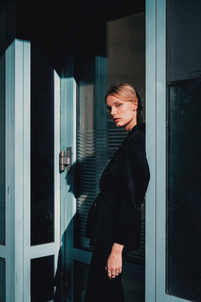 Staged Photography VS Candid Photography. Which one is best for you? Fedor Vasilev Photographer In Berlin A woman standing by a glass door staged portrait photograph by Fedor Vasilev
