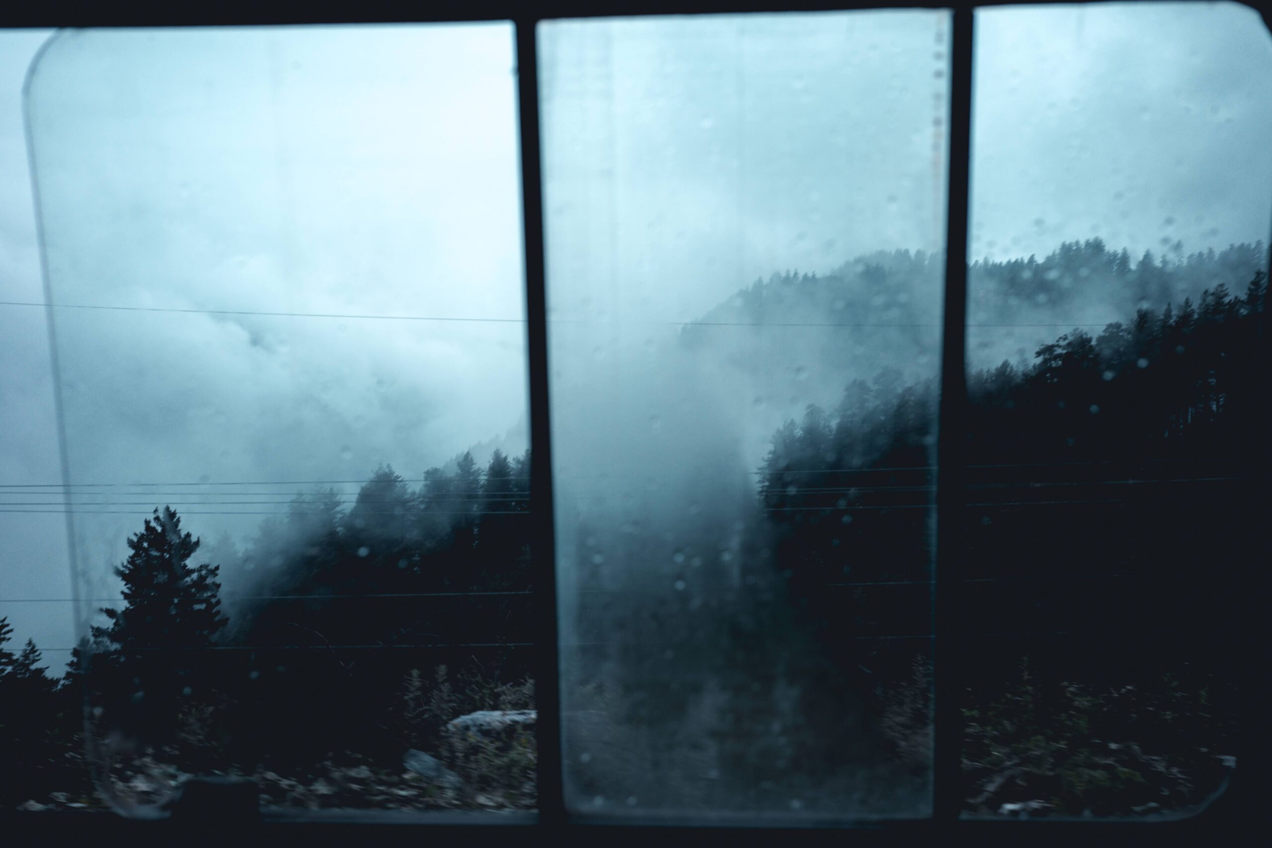 Photo essay about a trip to Georgia, a rainy view on mountains with pine tree forest through a window