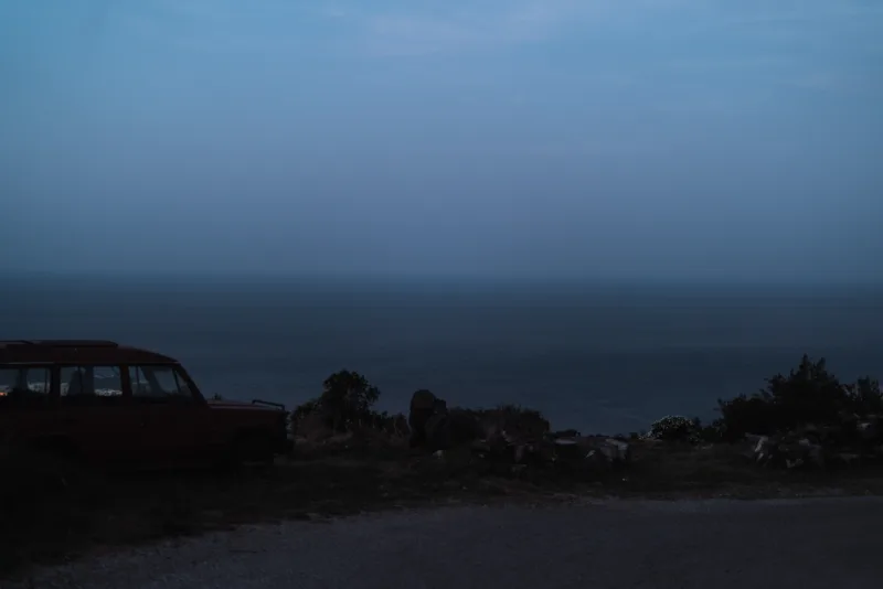 A car on a hill with the view over a sea at dusk