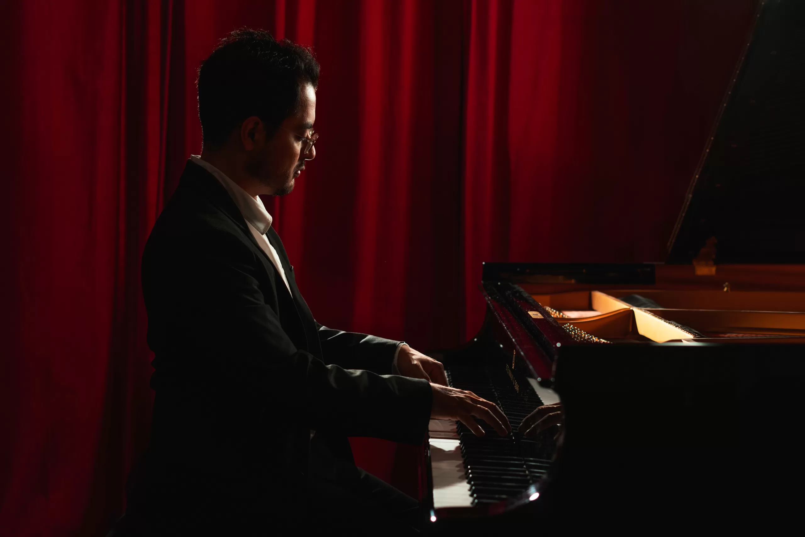 A pianist playing a piano in front of red curtains