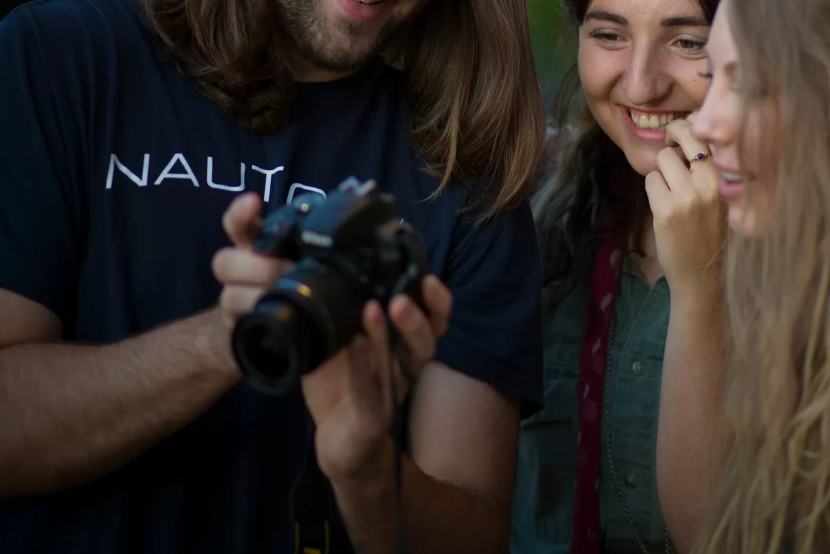 Group of students standing next to a photographer showing camera settings 