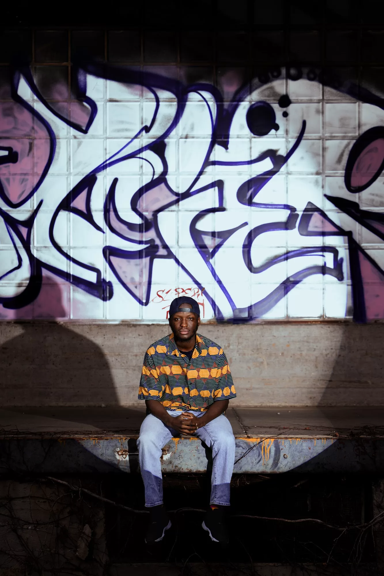 man in a spot of light sitting on a train station with graffiti