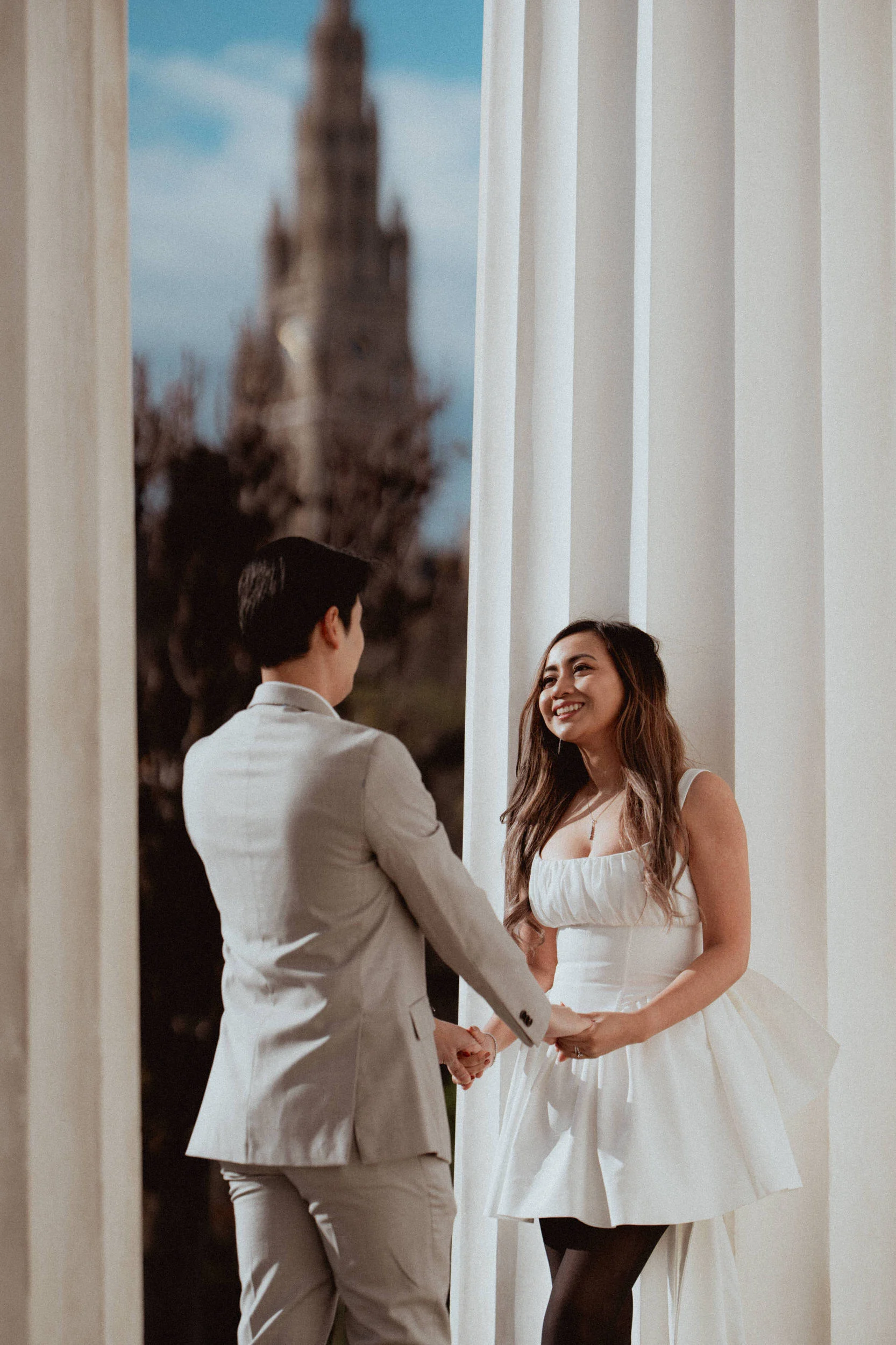 A couple standing holding hands with the tower of rathaus in Vienna