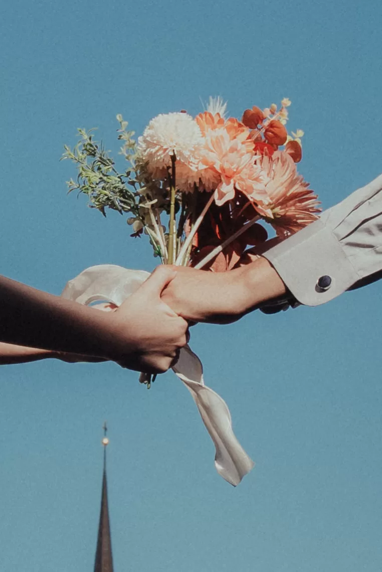 Photographer in Vienna Fedor Vasilev Photographer In Vienna hands holding a bouquet against a clear blue sky and a church roof in Vienna
