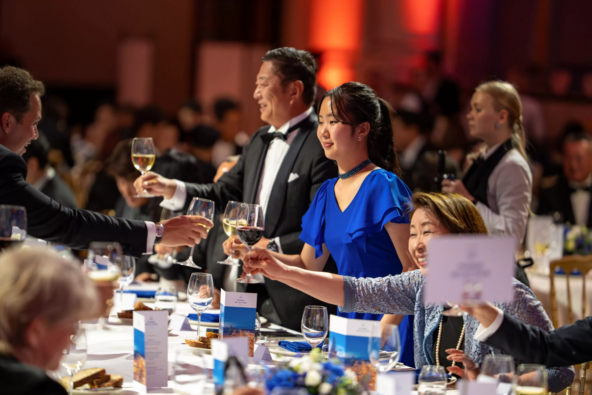 People Clinking glasses at a gala dinner at a big long table in a big event venue
