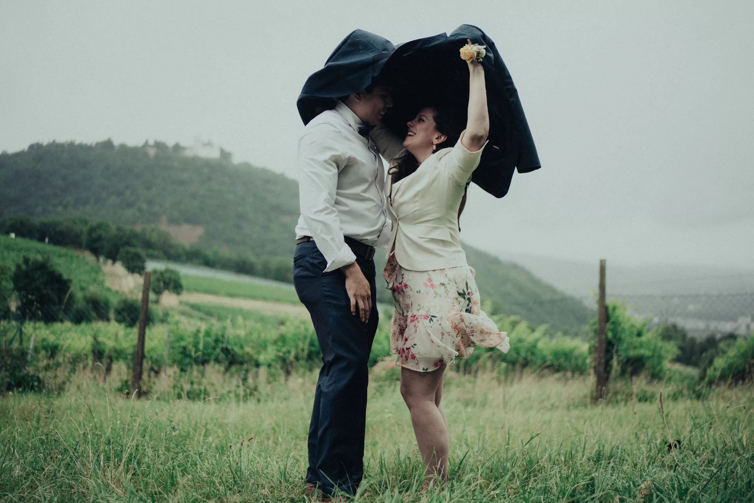 couple hiding from rain under a blazer standing on a field near kahlenberg
