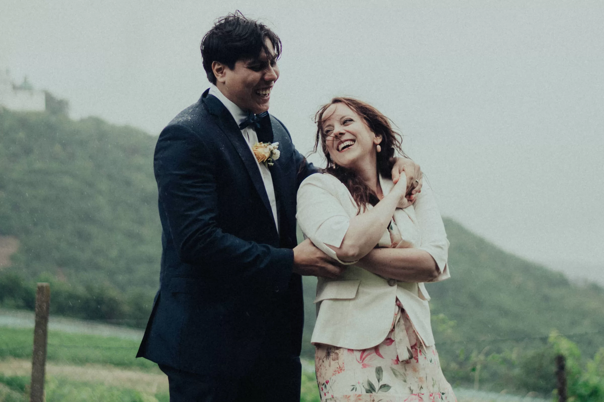 Photo from a wedding in Vienna on a rainy day. A couple hugging on Kahlenberg surrounded by vineyards