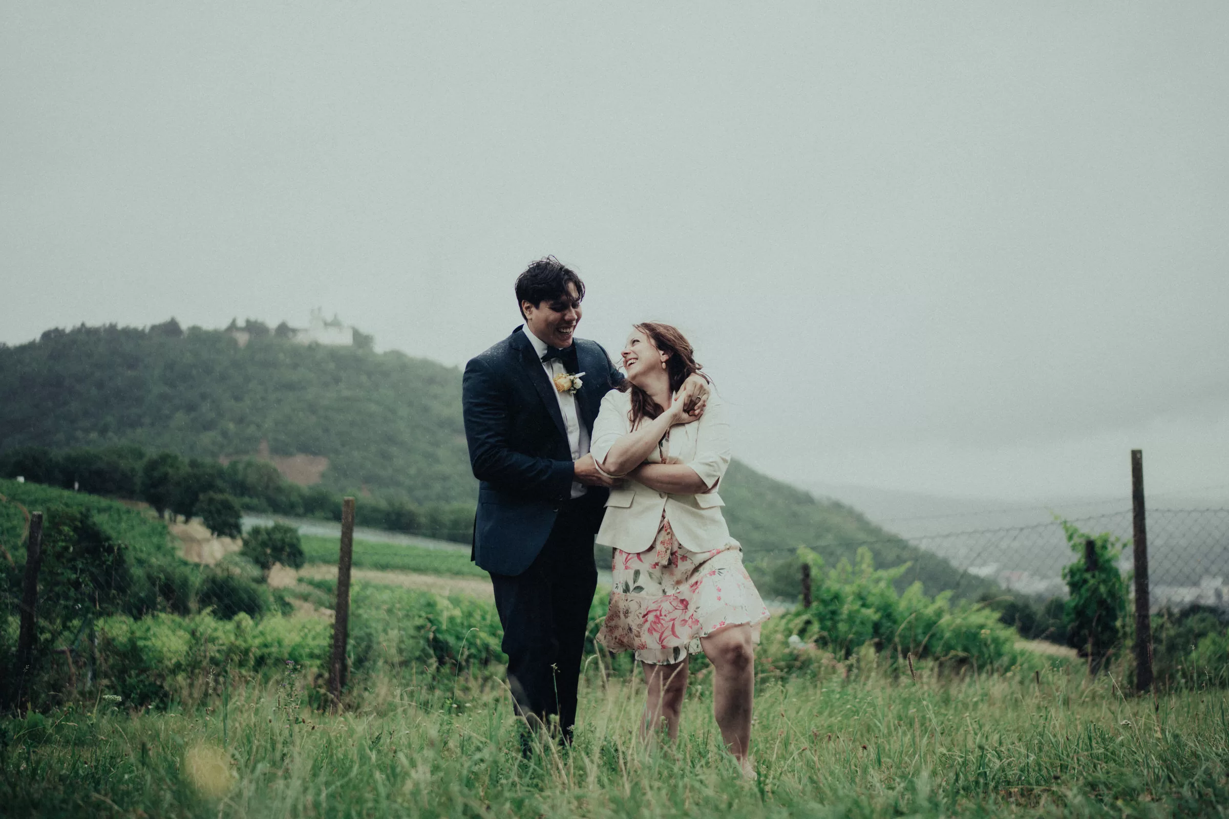 a couple stands in a field on their wedding hugging on a rainy day