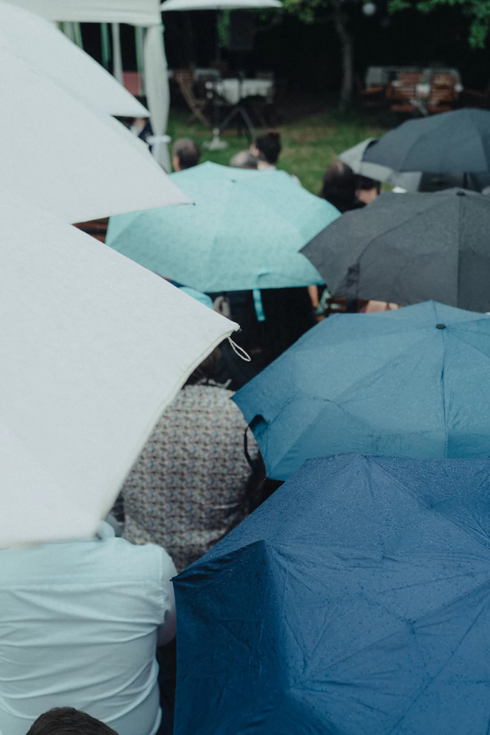 Guests of a wedding in a garden sitting under umbrellas during ceremony