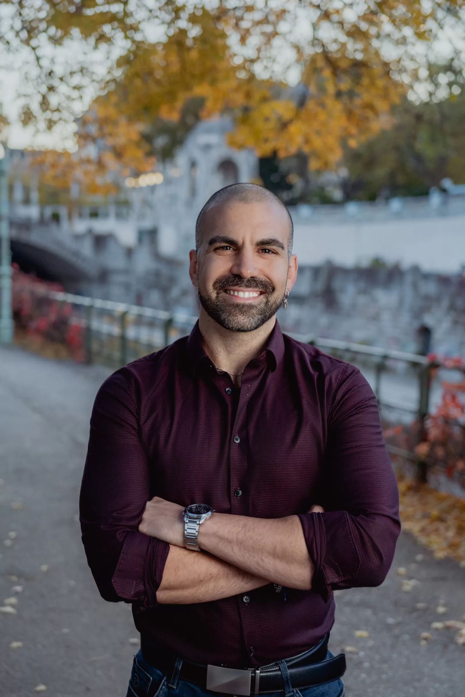Portrait of a smiling man in a red shirt standing in a park under a tree