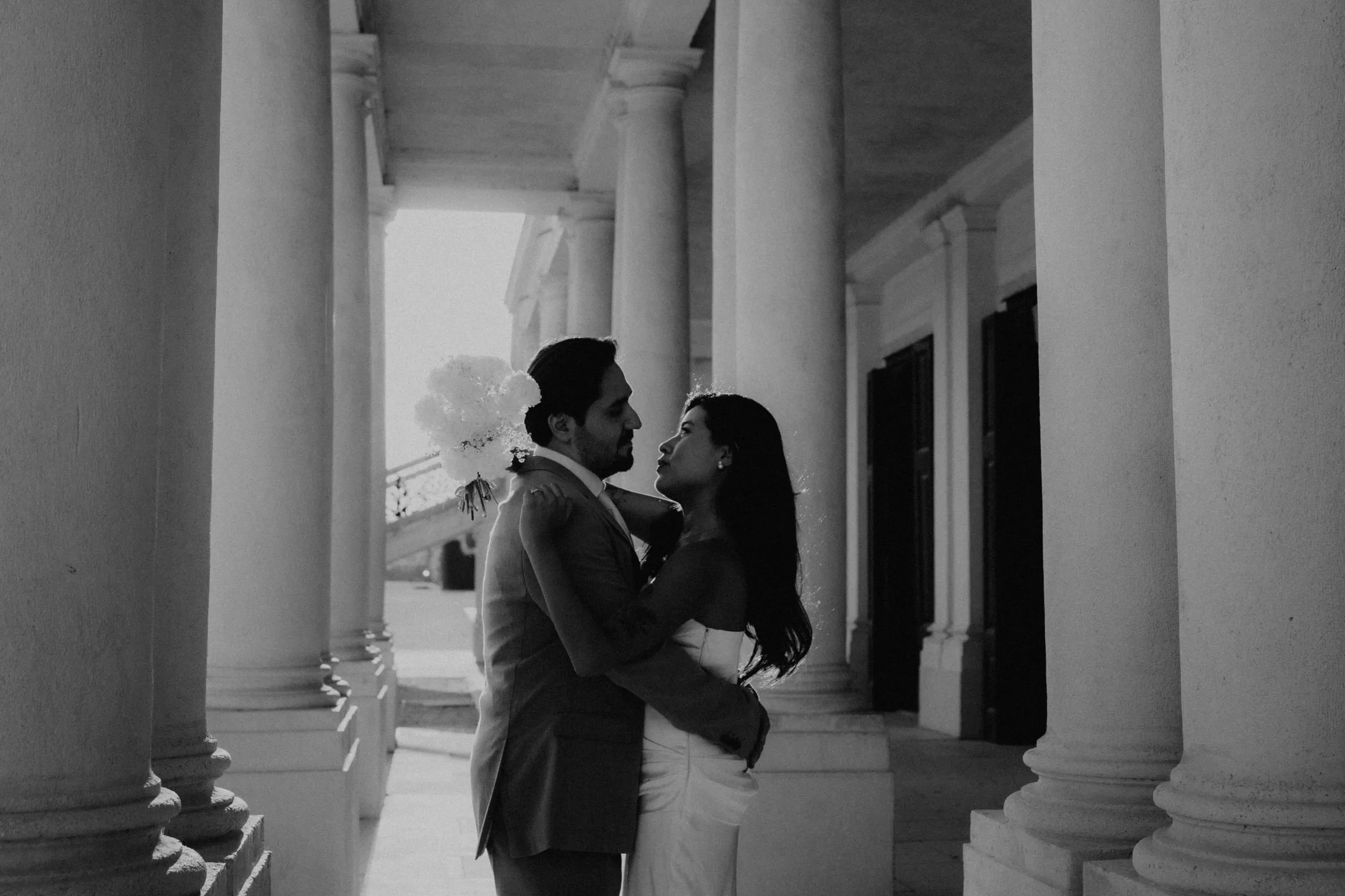 Black and white photo of a couple hugging under columns of schoenbrunn from an engagement session in Vienna