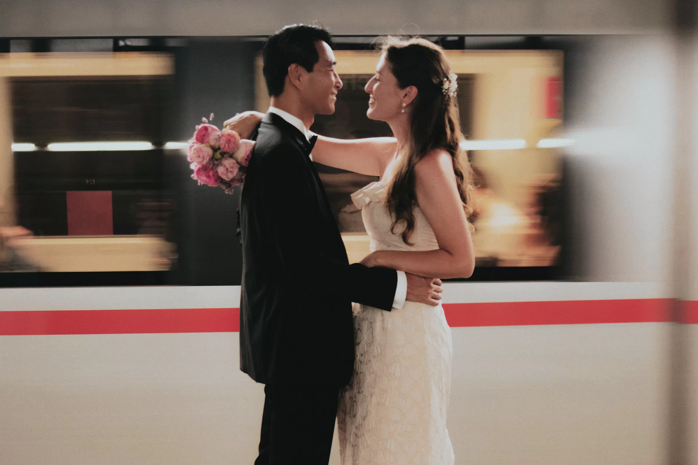 Couple hugging and looking at each other with a train passing in the background in Vienna