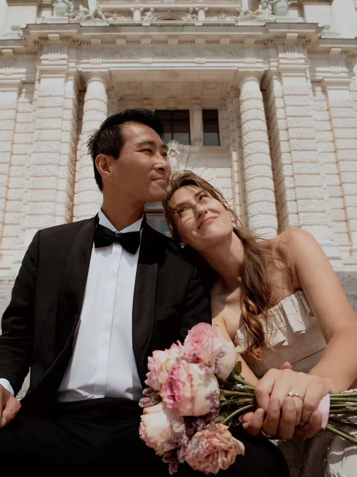 A couple sitting on the stairs of Hofburg In vienna with a bouquet on their wedding photoshoot