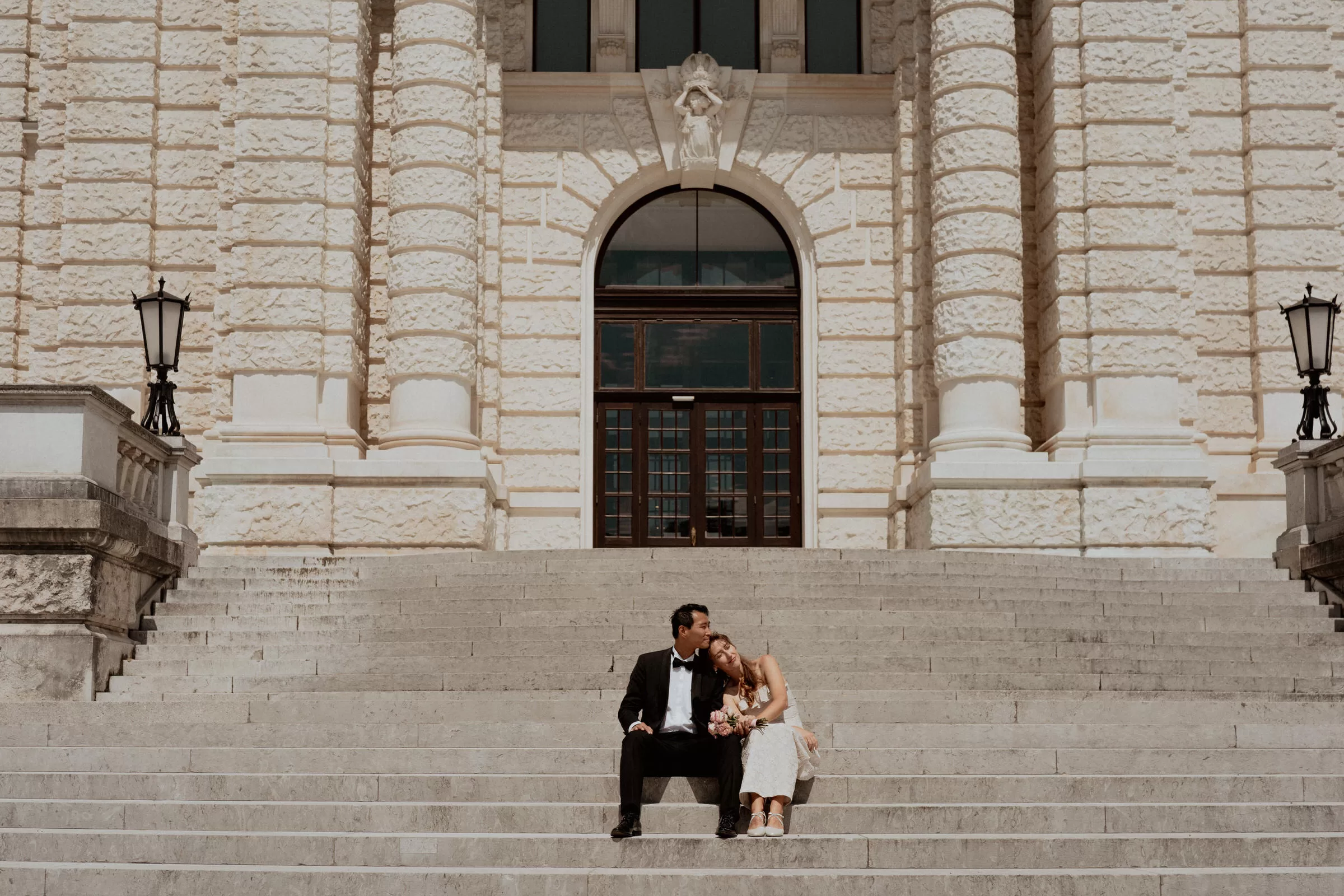Couple sitting on the stairs of hofburg from the side of Burggarten  leaning on each other