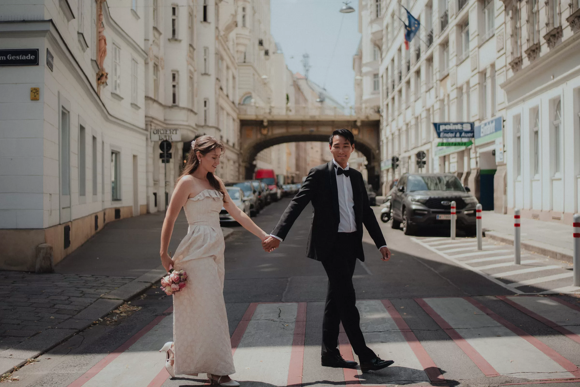 A couple walking across a street holding hands near Hohe Brücke, Vienna on a sunny day
