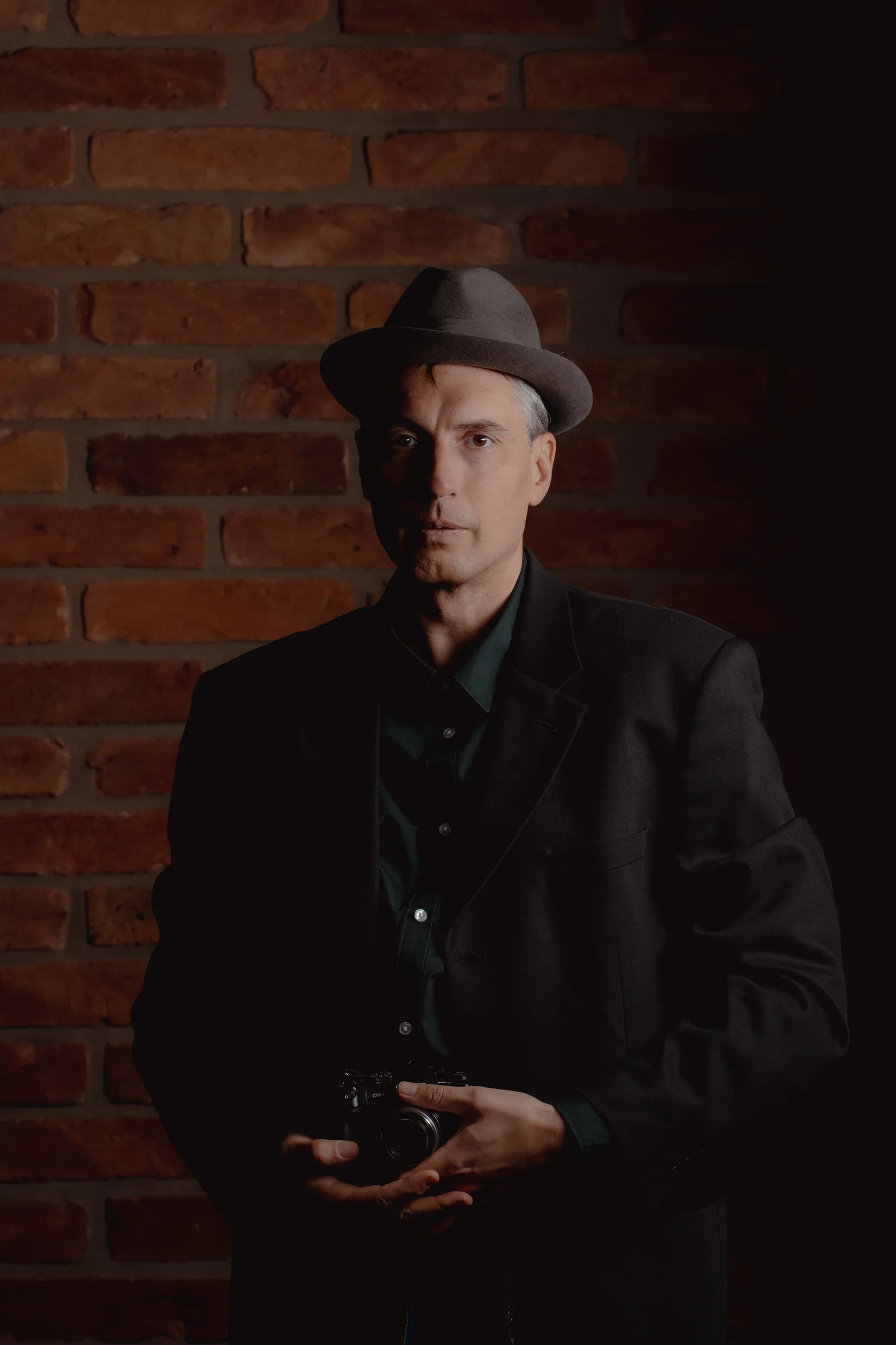 Artistic portrait of a man in a hat in front of a brick wall