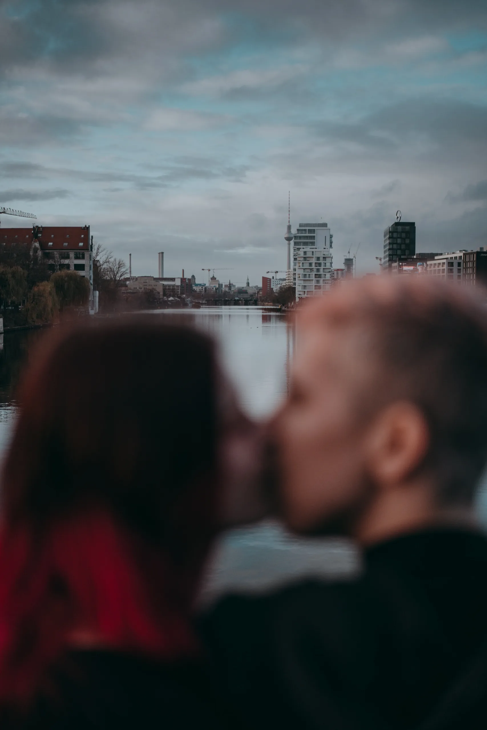a couple kissing with the view on Spree from Oberbaumbrücke on a sunny evening with berlin tv tower in the background