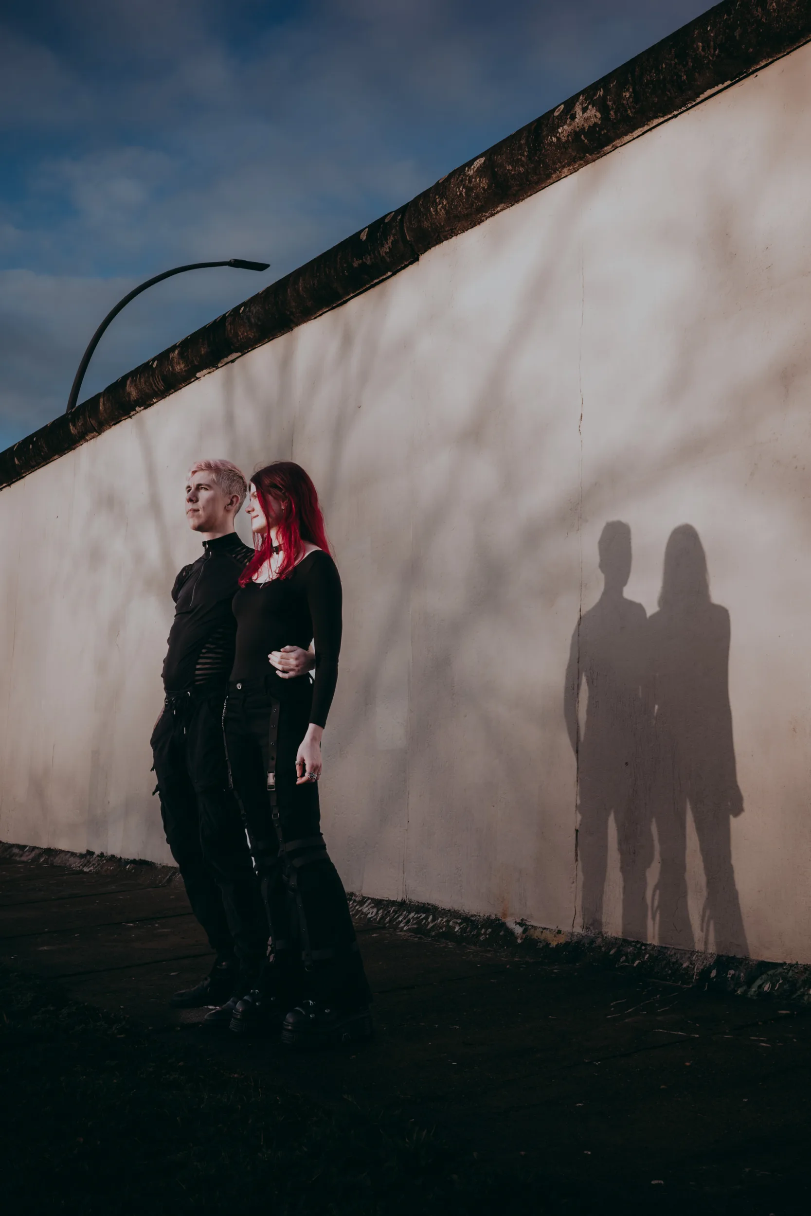 A dramatic photo of a couple stading in front of the berlin wall in Friedrichshain during golden hour on a sunny day