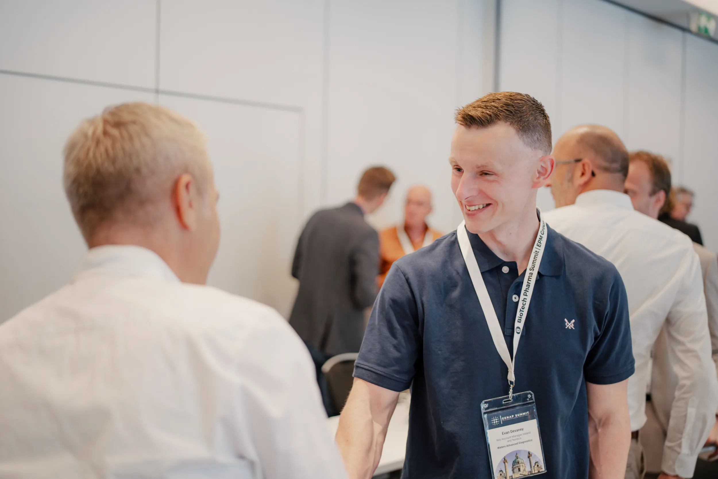 Genup Summit | Medical Conference Photography and Product Expo Fedor Vasilev Photographer In Berlin Smiling attendee wearing a Biotech Pharma Summit lanyard shakes hands with a colleague, captured by Fedor Vasilev.