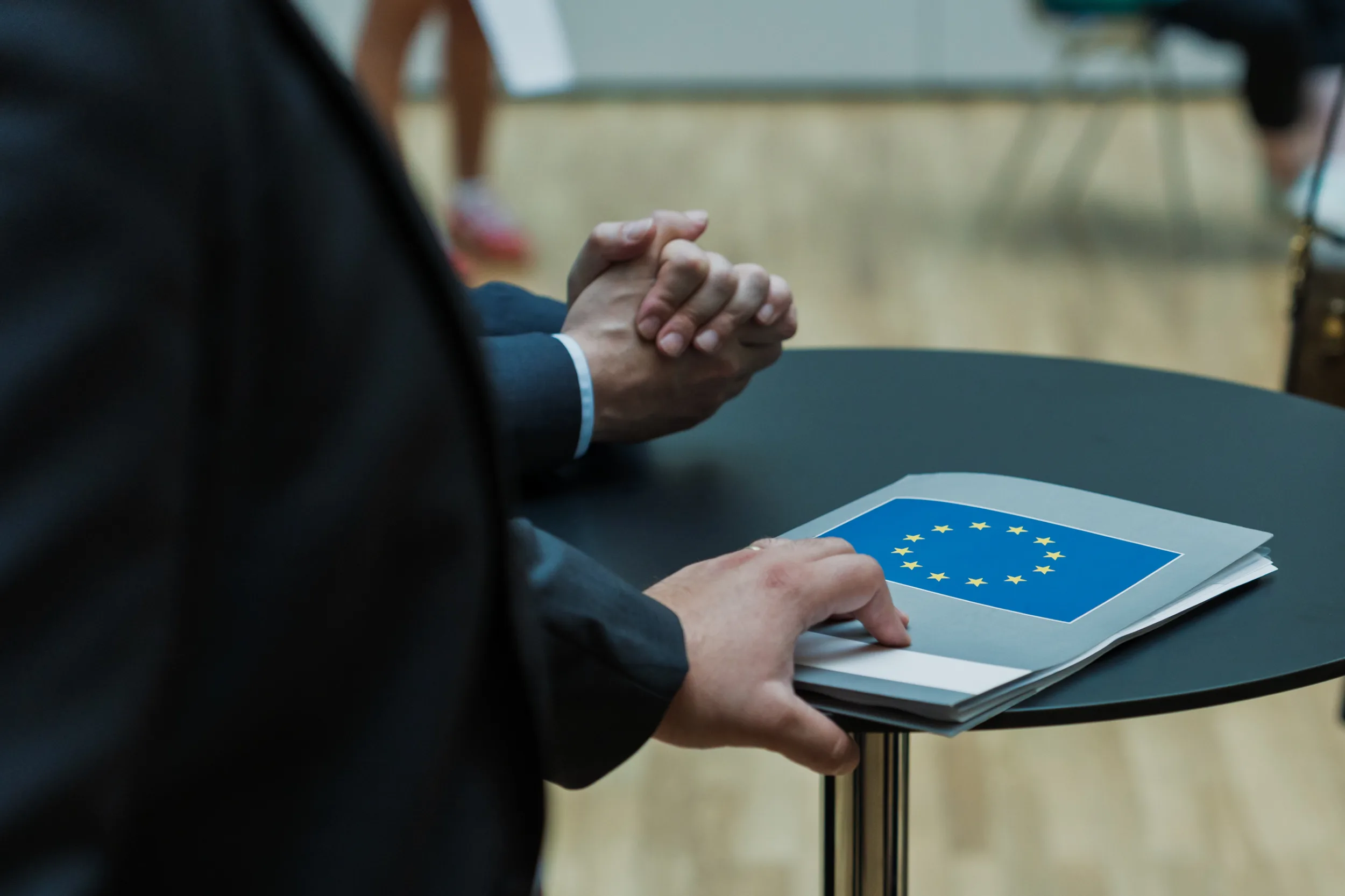 European Union Event Photographer | Grant Signing Ceremony in Vienna Fedor Vasilev Photographer In Berlin Close-up of a person resting a hand on a folder featuring the European Union star emblem on a round black table.