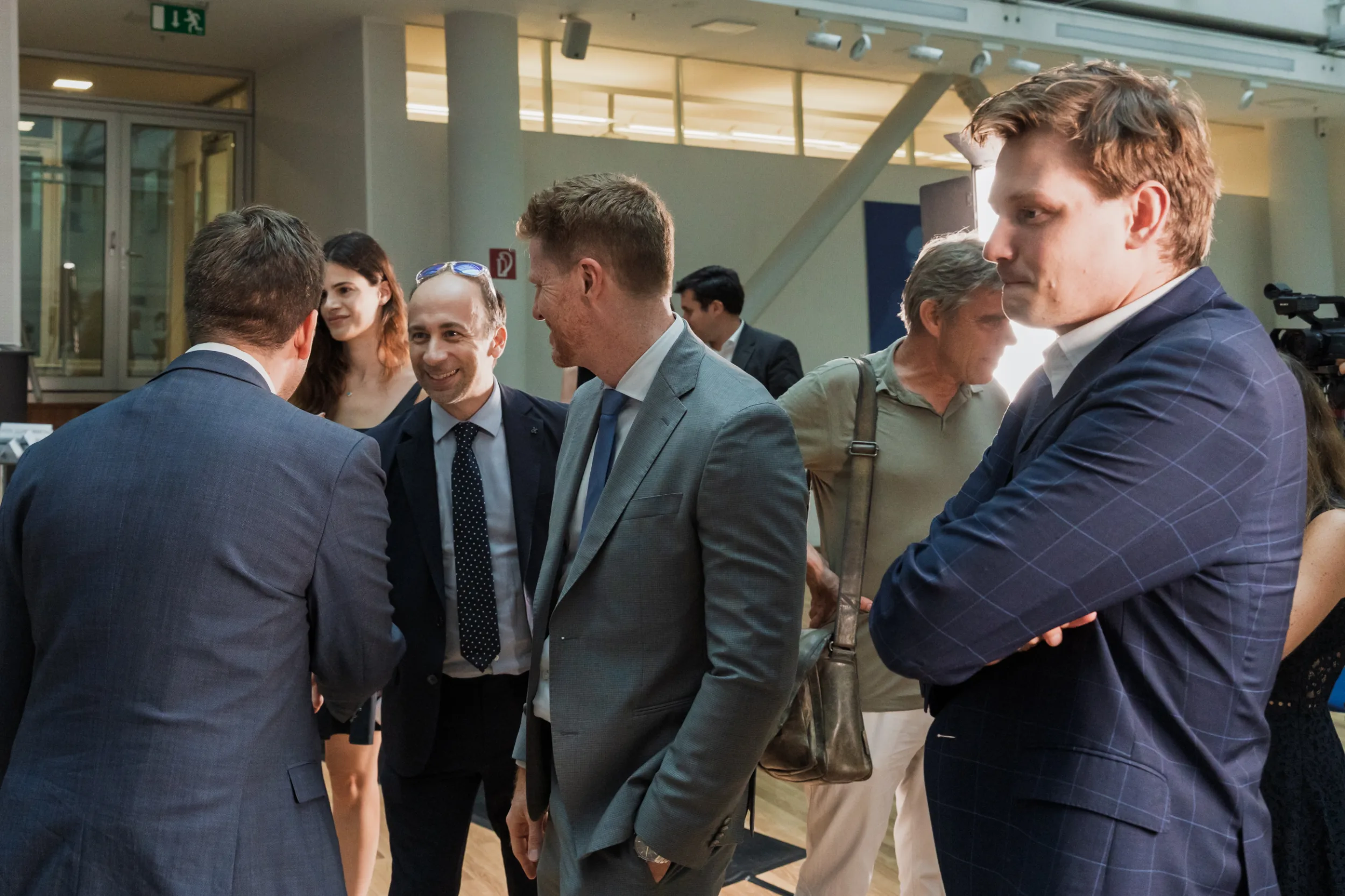 European Union Event Photographer | Grant Signing Ceremony in Vienna Fedor Vasilev Photographer In Berlin Business professionals mingle in a bright hall, focusing on a man in a grey suit laughing during a formal gathering.