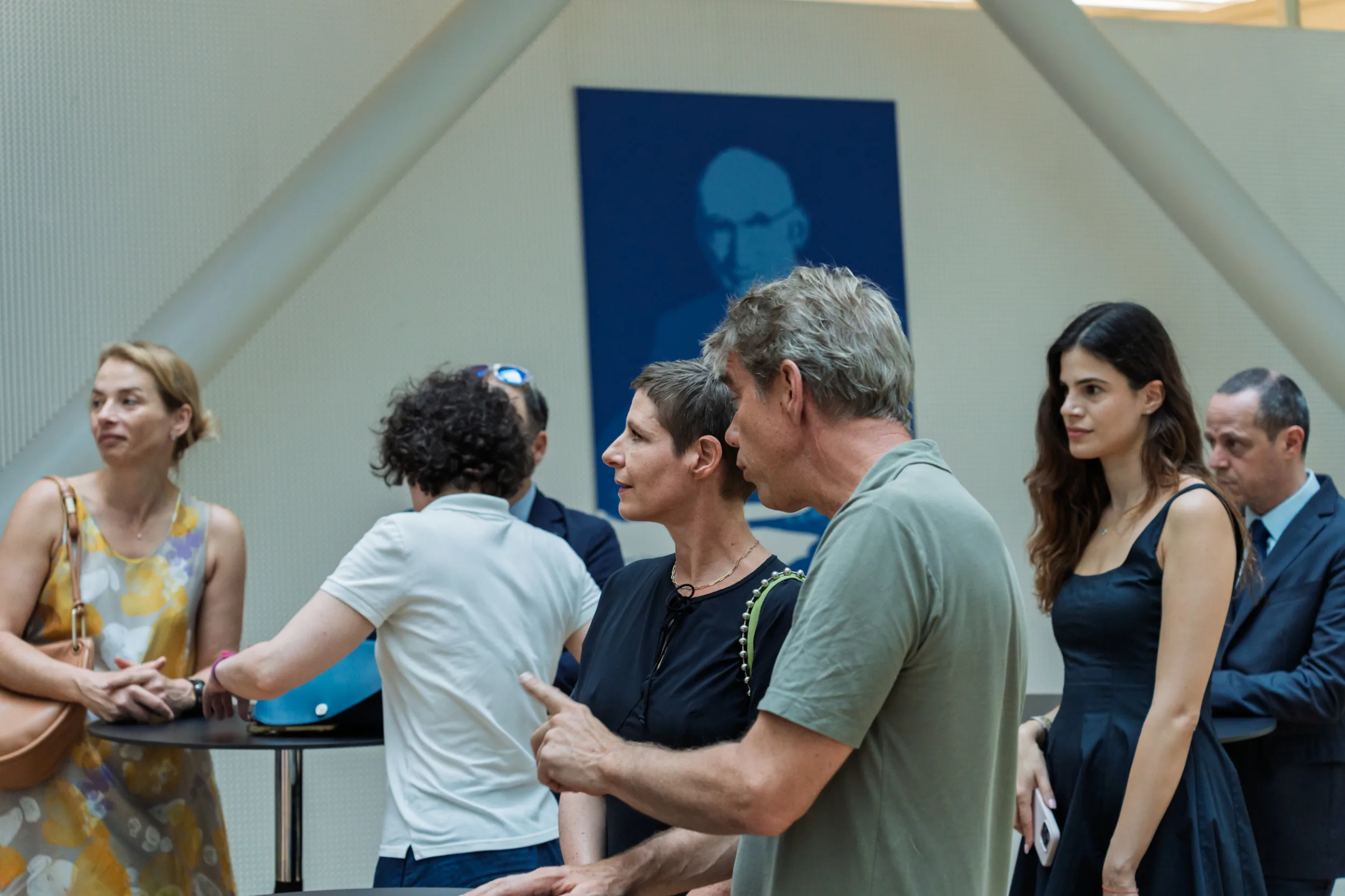 European Union Event Photographer | Grant Signing Ceremony in Vienna Fedor Vasilev Photographer In Berlin People in a modern interior space talking near a table with a blue portrait of a man on the wall behind them.
