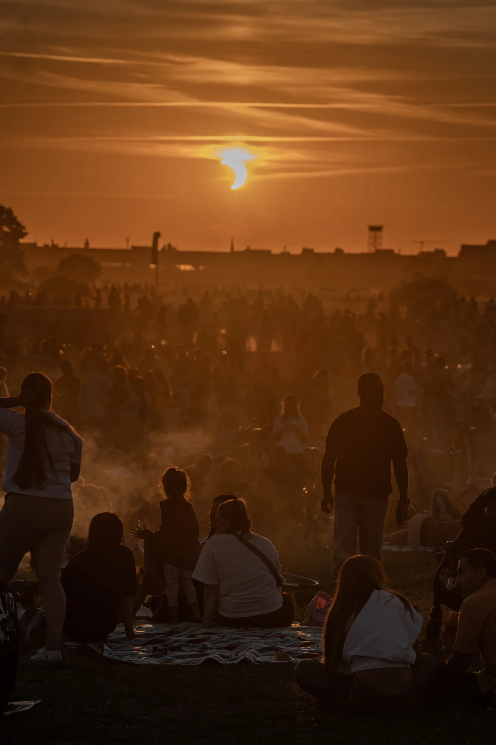 Photographing the Solar Eclipse in Berlin Fedor Vasilev Photographer In Berlin Crowd gathered on a grassy field watches a partial solar eclipse against a warm, hazy golden sunset.