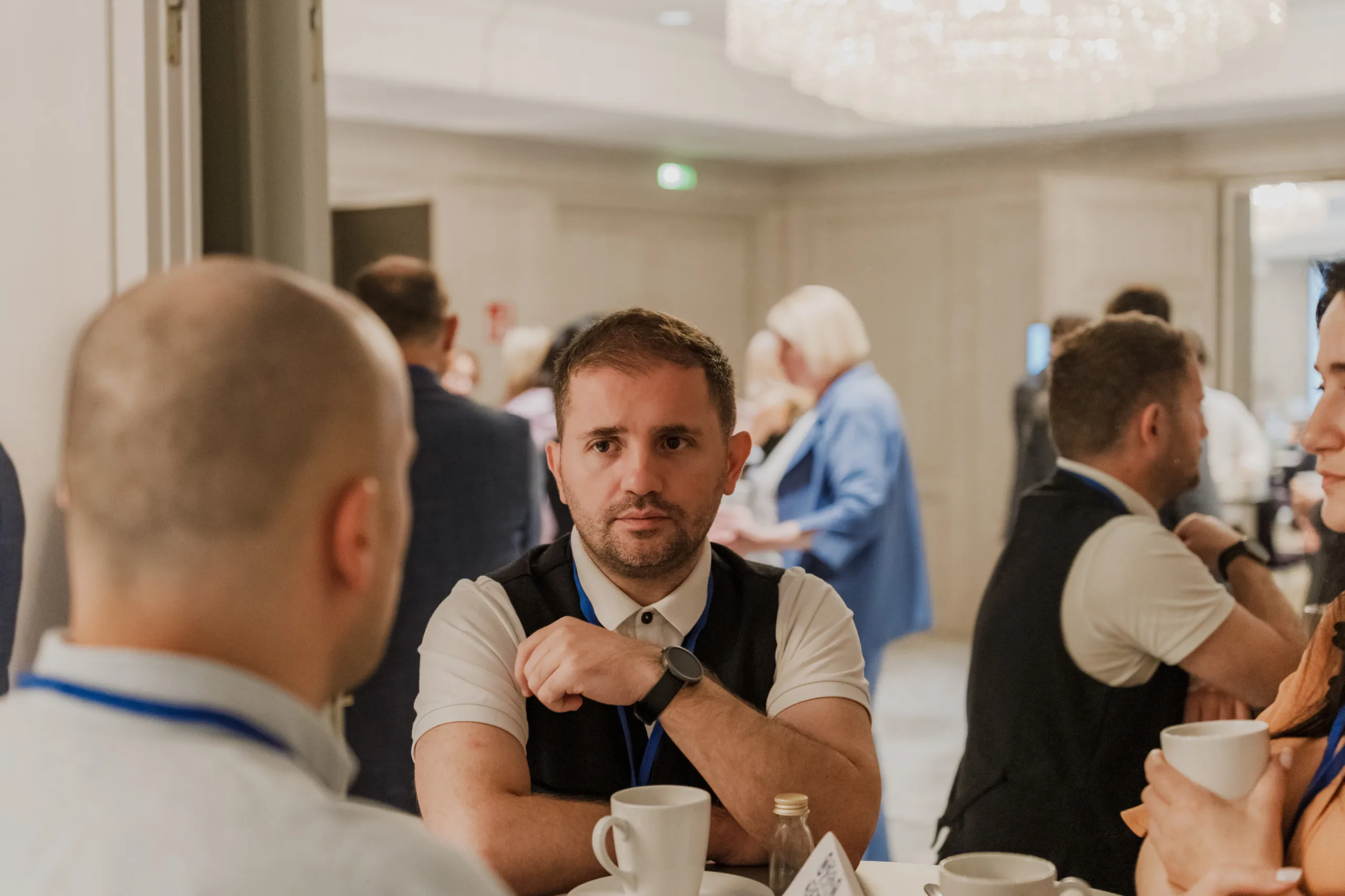 EU4Energy Conference Photography in Vienna Fedor Vasilev Photographer In Berlin Man wearing a dark vest and white polo shirt sits at a table during an EU4Energy event while looking at a colleague.
