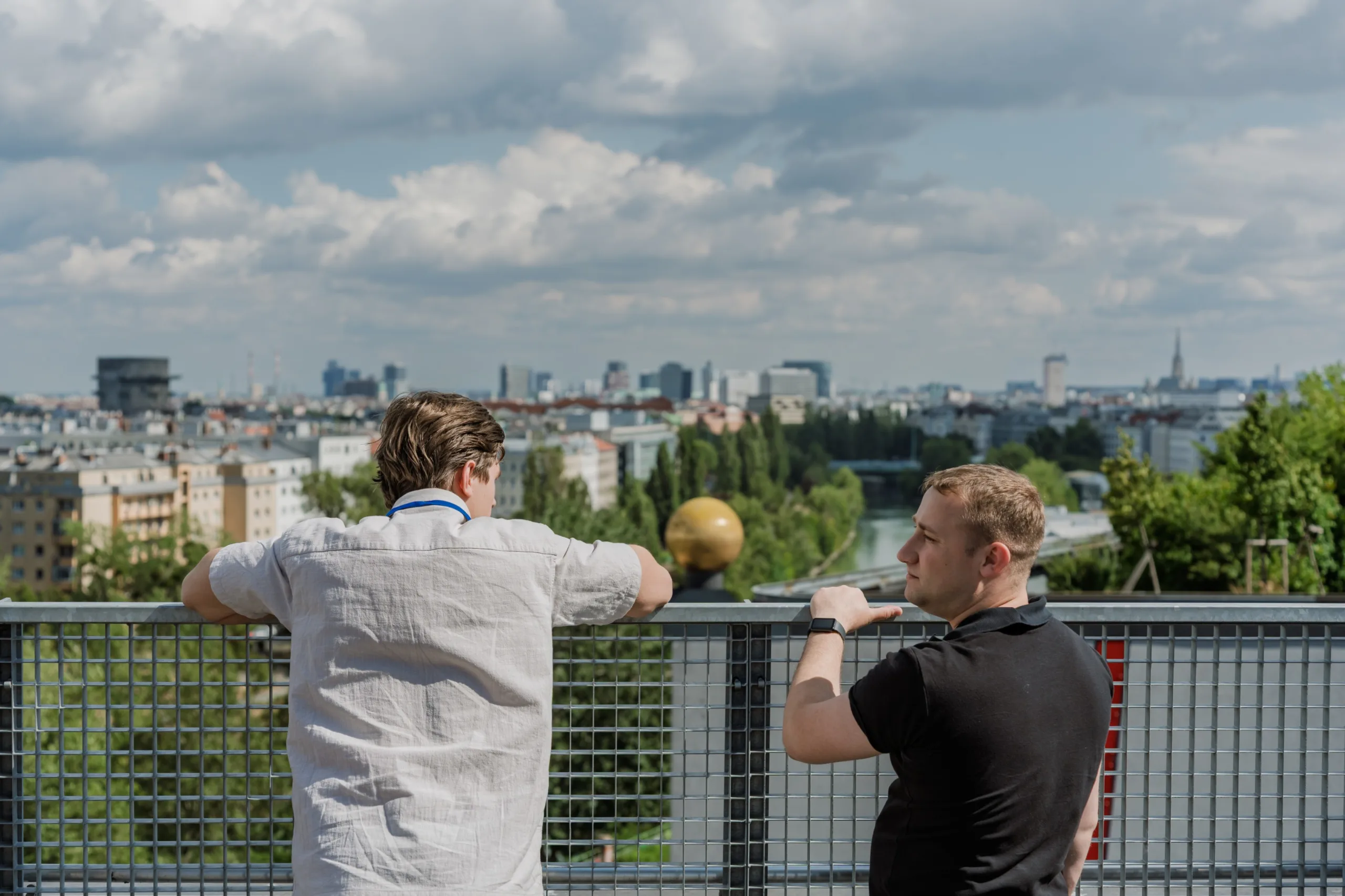 EU4Energy Conference Photography in Vienna Fedor Vasilev Photographer In Berlin Two men lean on a metal railing overlooking a cityscape on a cloudy day during a break from the EU4Energy conference.