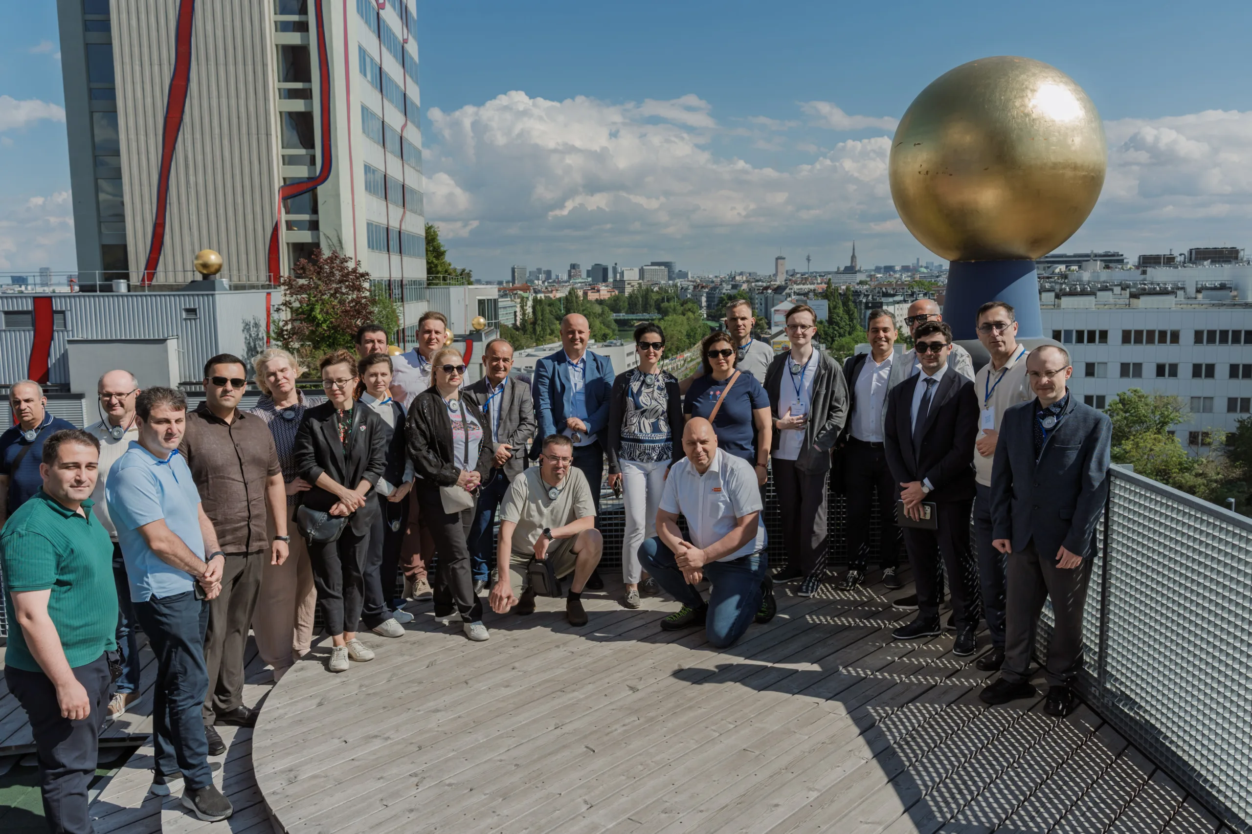 EU4Energy Conference Photography in Vienna Fedor Vasilev Photographer In Berlin Group of conference attendees posing on a sunny rooftop terrace next to a large golden sphere sculpture.