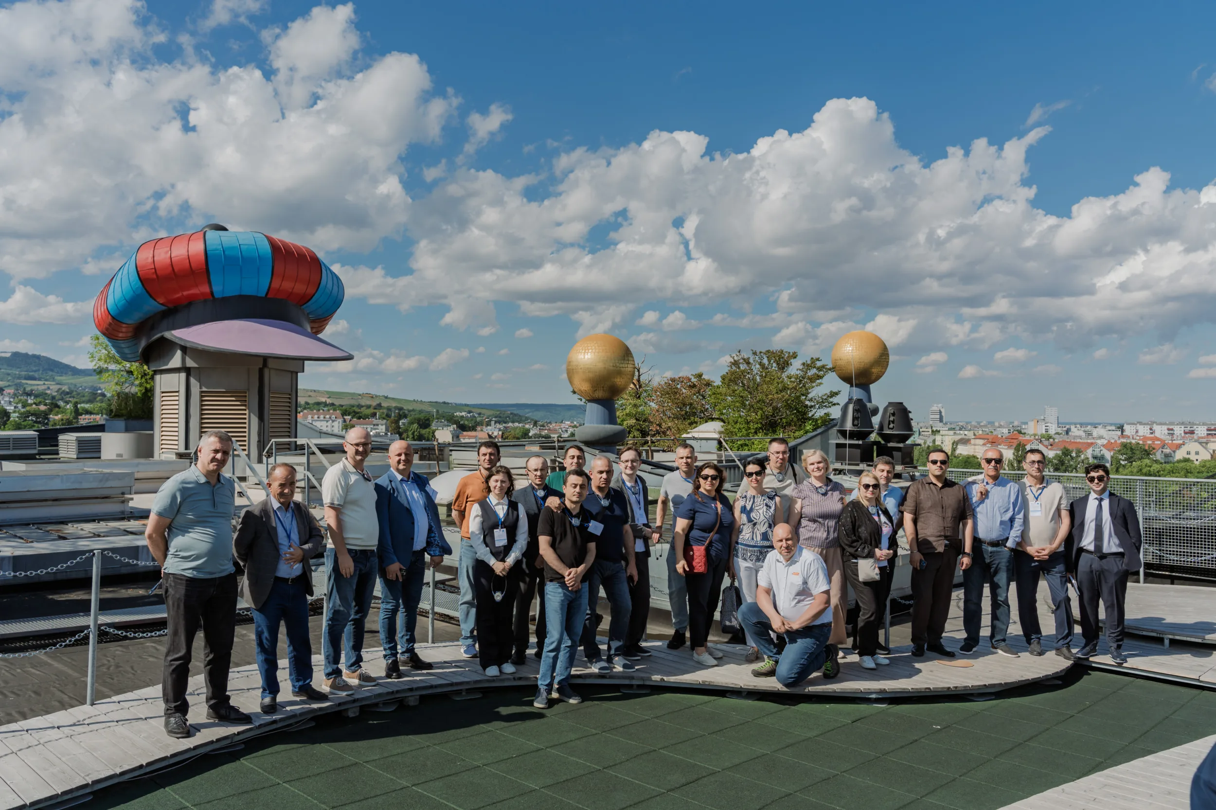 EU4Energy Conference Photography in Vienna Fedor Vasilev Photographer In Berlin Large group of conference attendees posing together on a sunlit rooftop terrace under a bright blue sky.