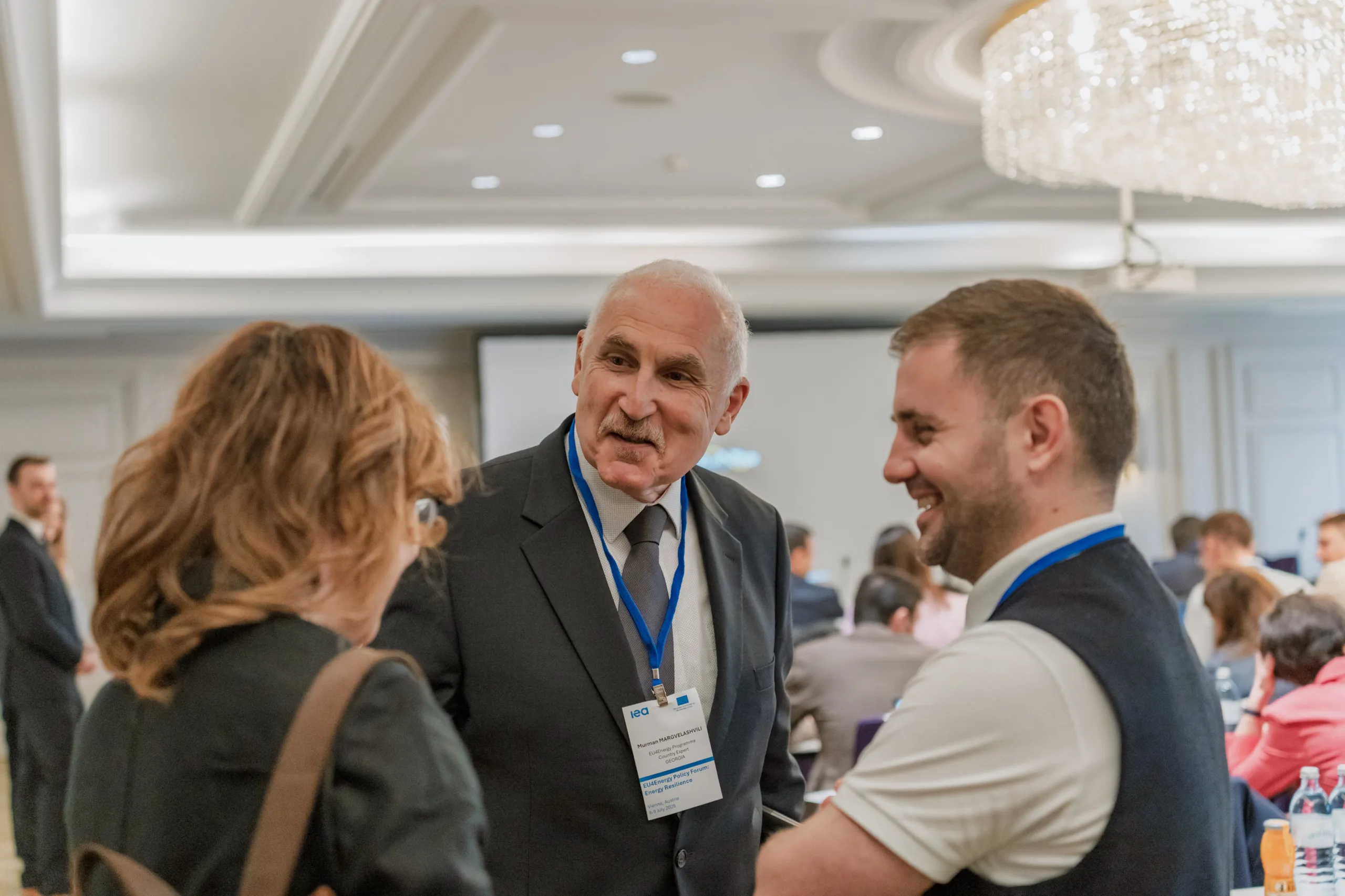 EU4Energy Conference Photography in Vienna Fedor Vasilev Photographer In Berlin Senior professional with a grey tie and IEA badge speaks with colleagues during the EU4Energy conference networking.