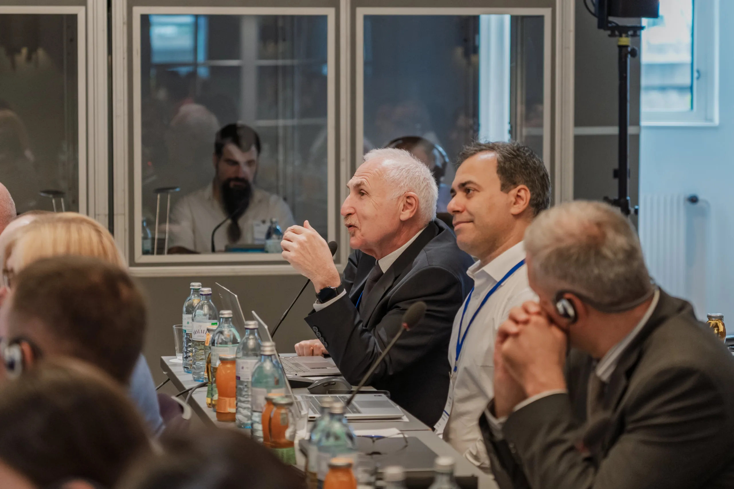 EU4Energy Conference Photography in Vienna Fedor Vasilev Photographer In Berlin Elderly man gestures while speaking into a microphone during a seminar with attendees wearing translation headsets.