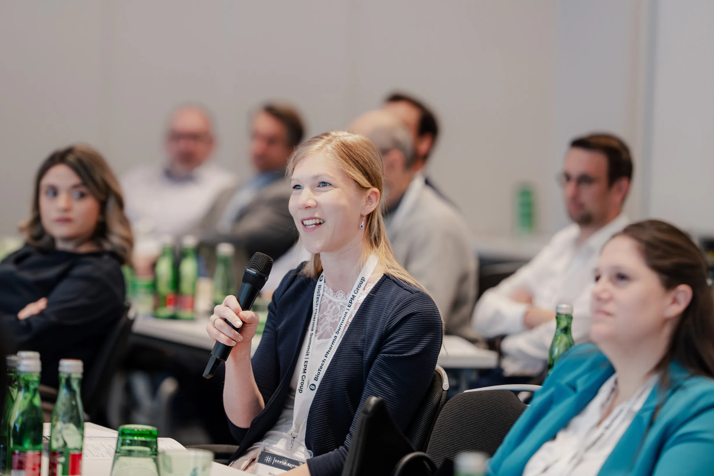 Genup Summit | Medical Conference Photography and Product Expo Fedor Vasilev Photographer In Berlin Smiling blonde woman holding a microphone to ask a question during a professional conference session.