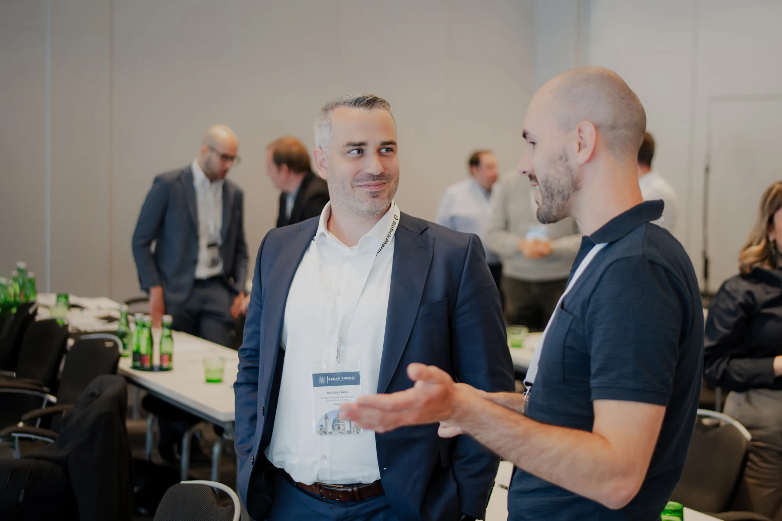 Genup Summit | Medical Conference Photography and Product Expo Fedor Vasilev Photographer In Berlin Two men in business attire engage in a conversation at the Genup Summit conference while wearing event name badges.