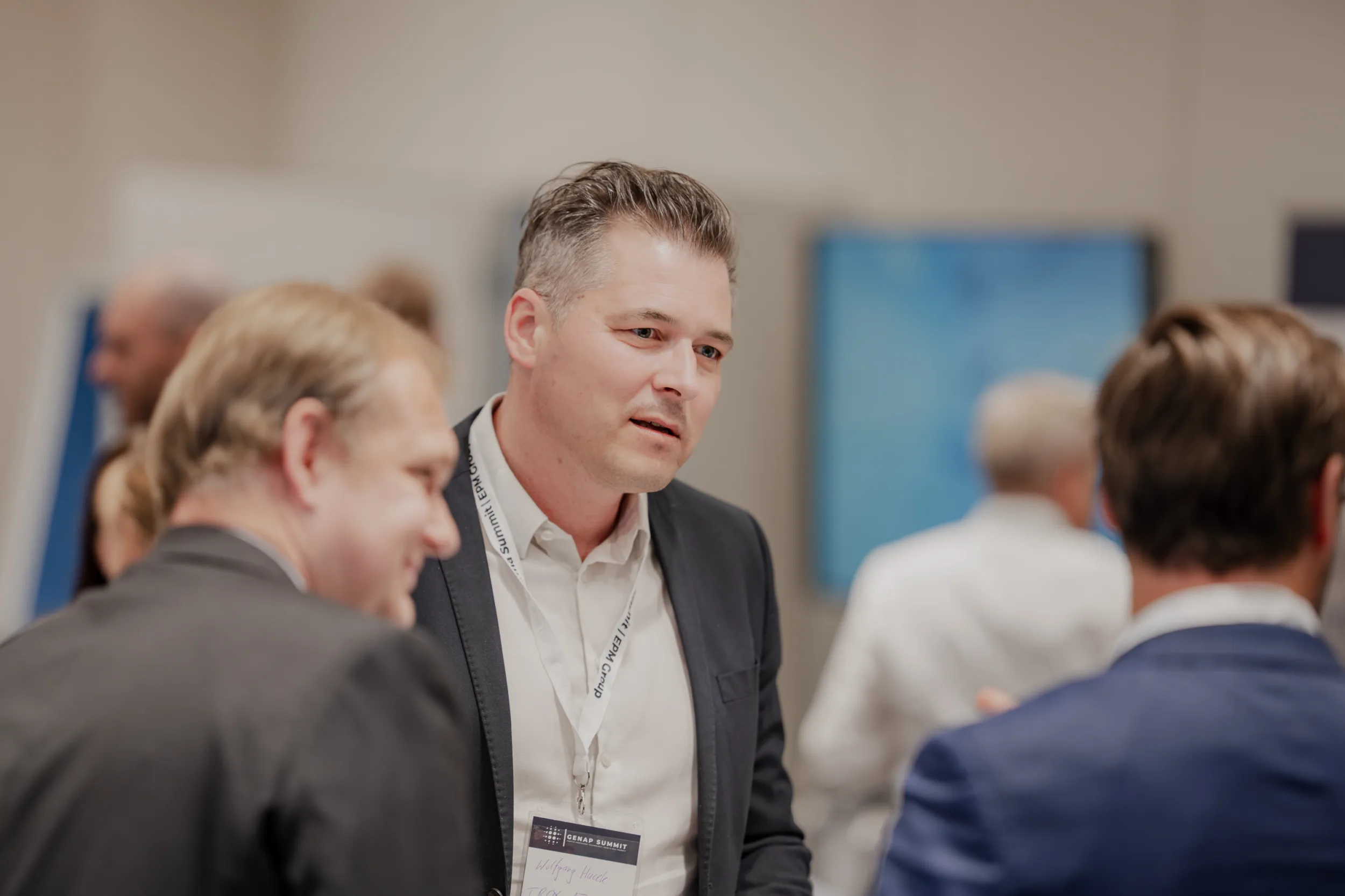 Genup Summit | Medical Conference Photography and Product Expo Fedor Vasilev Photographer In Berlin Attendee with a Genup Summit lanyard engaged in conversation with colleagues at a professional conference.