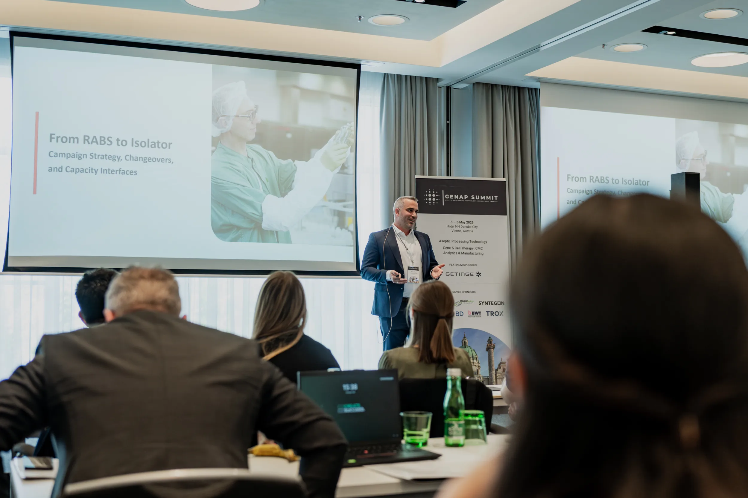 Genup Summit | Medical Conference Photography and Product Expo Fedor Vasilev Photographer In Berlin A speaker presenting on stage during a conference in a hotel room