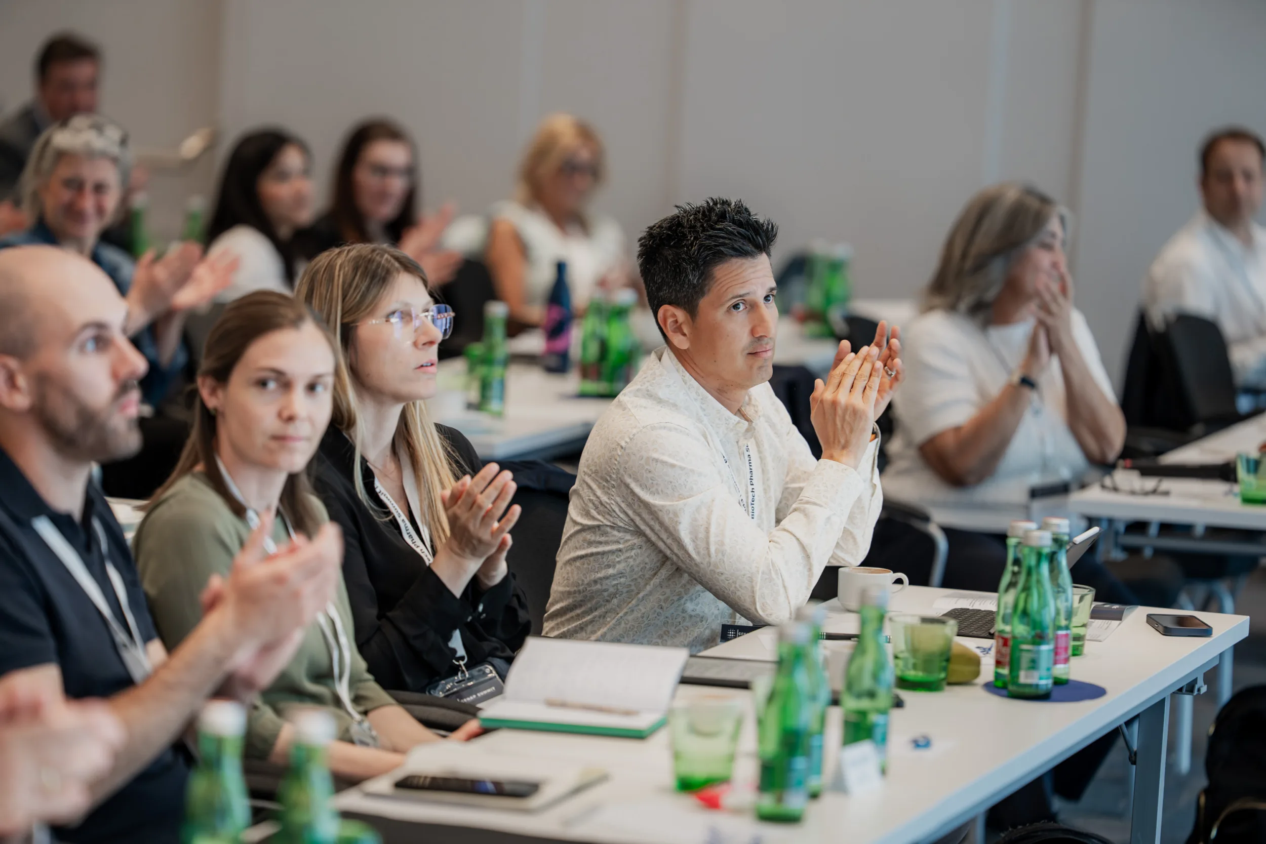 Genup Summit | Medical Conference Photography and Product Expo Fedor Vasilev Photographer In Berlin Audience members clapping at a conference while seated at tables with green water bottles.