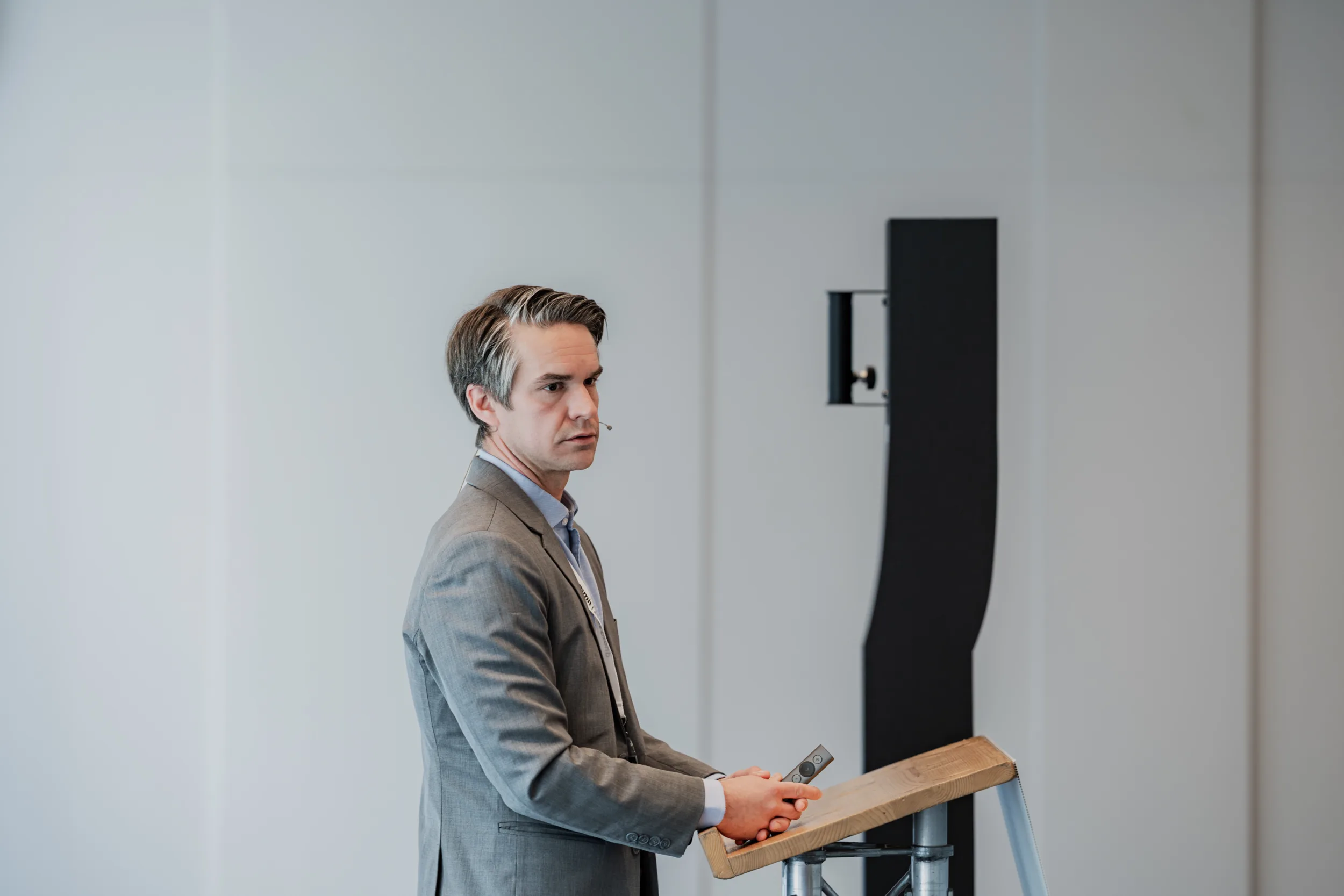 Genup Summit | Medical Conference Photography and Product Expo Fedor Vasilev Photographer In Berlin Man in a grey suit holding a presentation remote while standing at a wooden lectern during a conference
