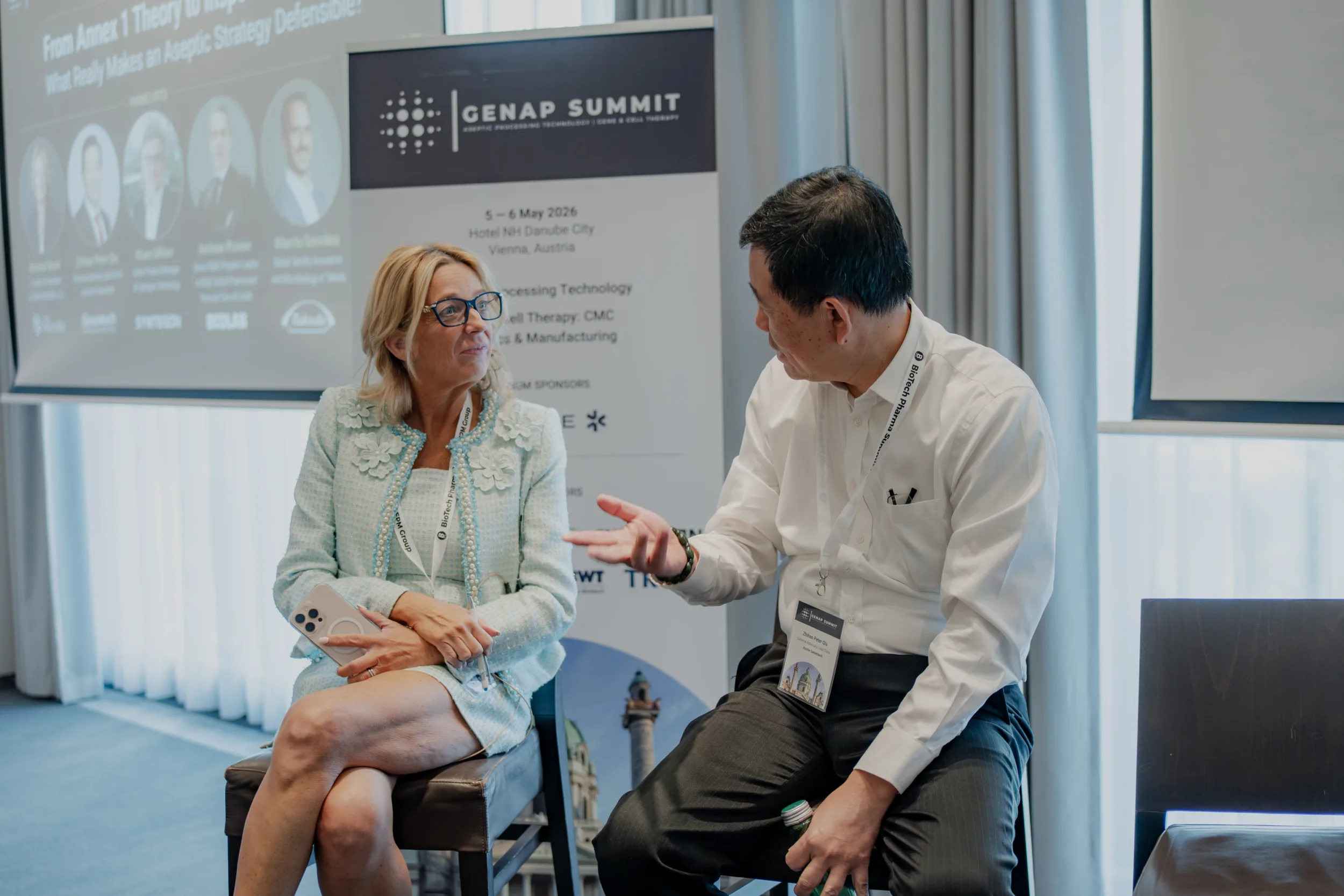 Genup Summit | Medical Conference Photography and Product Expo Fedor Vasilev Photographer In Berlin Man in a white shirt gestures while talking to a blonde woman in a light blue textured jacket at Genap Summit.